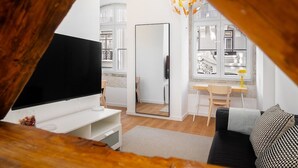 A modern living room with a flat-screen TV, a wooden dining table, a black sofa, and a large mirror. - Lisbon Living Redefined: Exclusive Downtown Spot (Lisboa)