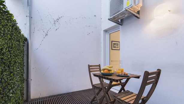 Un petit espace extérieur aménagé avec une table et des chaises, un saladier rempli de fruits et un verre de jus d’orange.