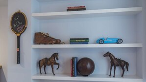 A shelf with a golf club, a pair of shoes, a book titled 'World of Golf', a blue toy car, and two horse figurines. - Tennis Room - Clean & Safe (Lisboa)