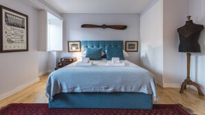 A bedroom with a large bed, a wooden headboard, a red patterned rug, and a mannequin on a stand. - Tennis Room - Clean & Safe (Lisboa)