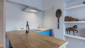 A modern kitchen with a wooden table, wine glasses, a bottle of wine, a sink, and a tennis racket on the wall. - Tennis Room - Clean & Safe (Lisboa)