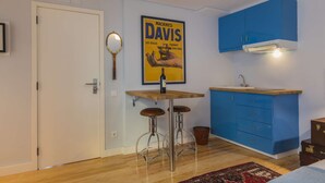 Eine kompakte Küche mit einem blauen Schrank, einem Holzbarhocker, einem Poster und einem kleinen Spülbecken.