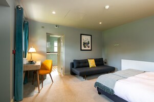 A hotel room with a bed, a sofa, a desk with a lamp, and a chair.