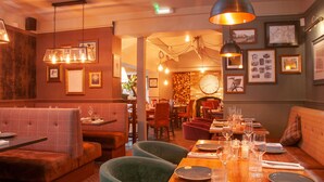 A restaurant with a wooden dining table set for a meal, cushioned seating, and hanging pendant lights.