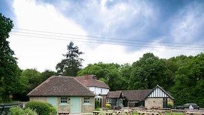 A rustic outdoor seating area with picnic tables, surrounded by traditional buildings with stone walls and pitched roofs.