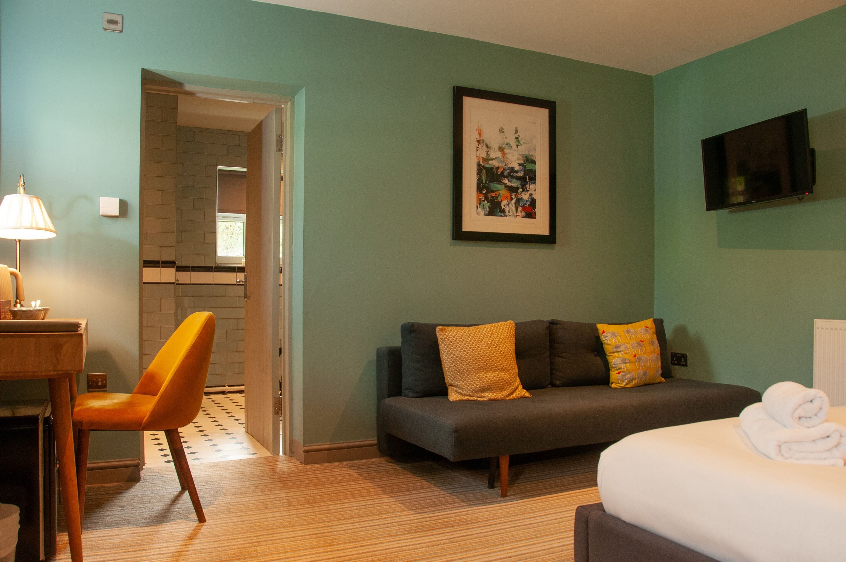 A hotel room with a sofa, a chair, a bed, a TV, and a framed picture on the wall.