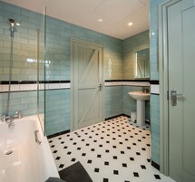 A bathroom with a white bathtub, a sink, and a glass shower enclosure. The floor has a black and white checkered pattern.