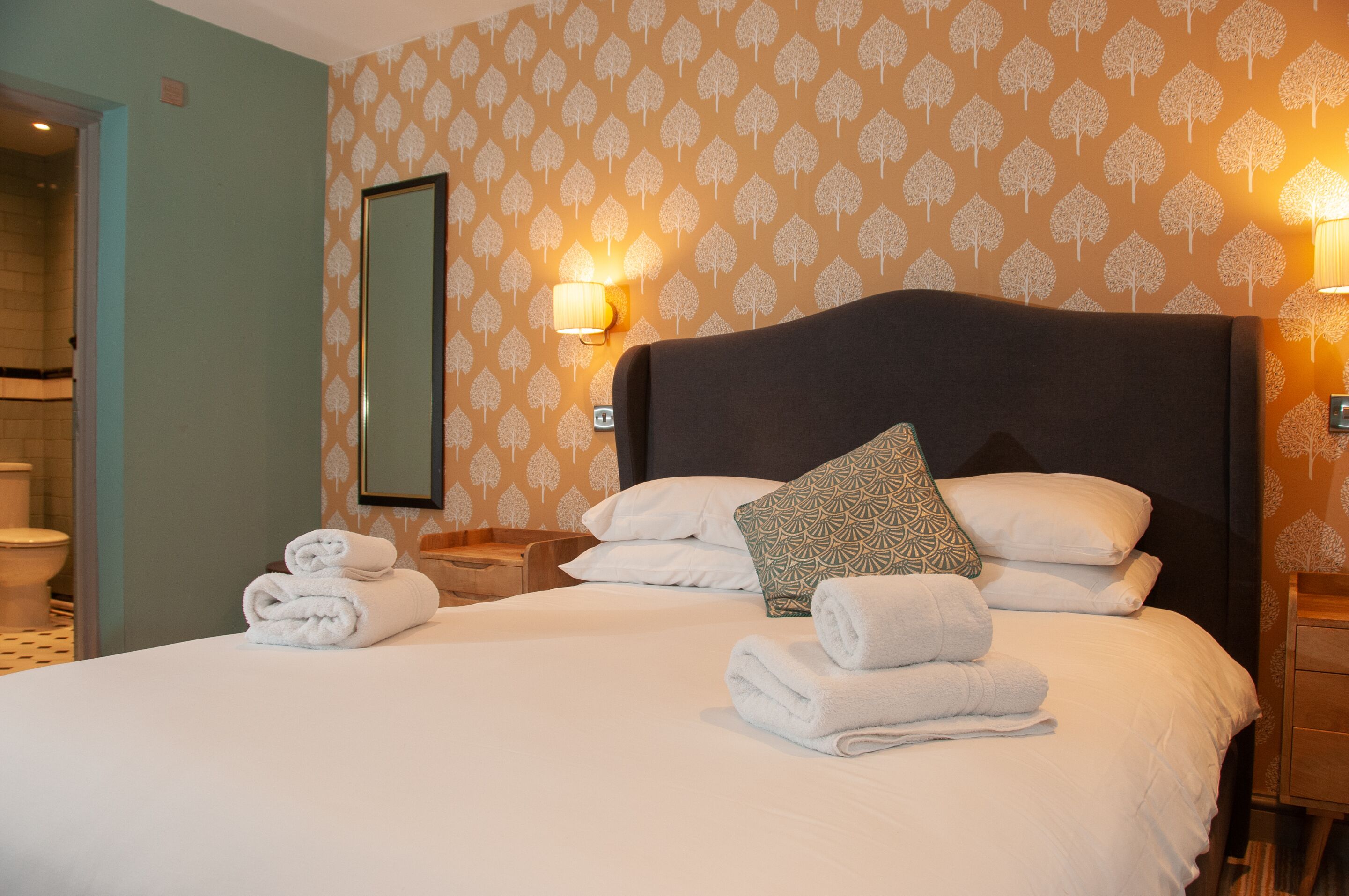 A hotel room with a large bed, two bedside tables, a mirror, and patterned wallpaper.