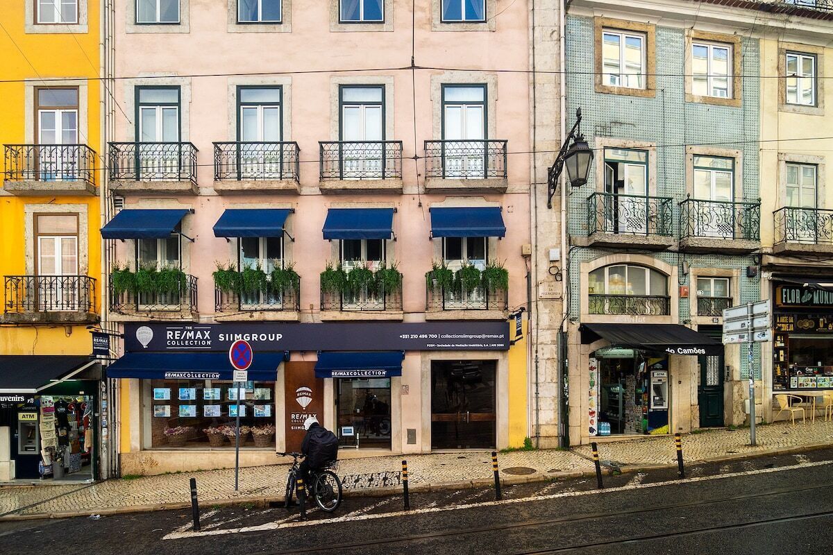 Um edifício com várias varandas, uma loja com toldo azul e uma pessoa andando de bicicleta.