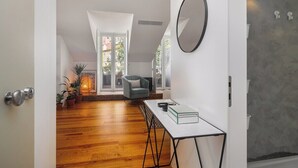 Een modern interieur met een houten vloer, een witte tafel met een boek, een grijze fauteuil en een grote spiegel aan de muur.