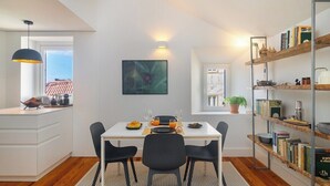 Een moderne eetruimte met een witte tafel, zwarte stoelen en een boekenkast met boeken en decoratieve objecten.