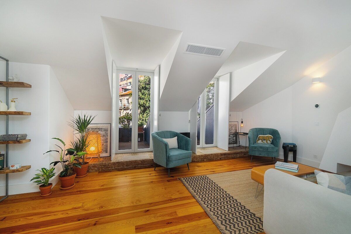 Un loft moderno con techo alto, suelo de madera y una zona de estar acogedora con sillones azul verdosos.