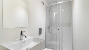 A modern bathroom with a large white sink, a mirror, and a glass-enclosed shower.