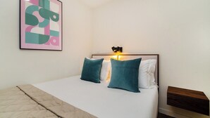 A neatly made bed with a quilt, two teal pillows, and a headboard with a light fixture.