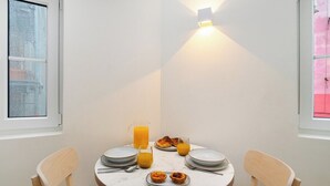 Una mesa de desayuno con platos, vasos y una jarra de jugo de naranja en una habitación con paredes blancas y un ventanal.