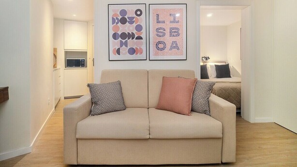 A modern living room with a beige sofa, two pillows, and abstract wall art. - Explore Lisbon from a Cozy Base in Alfama (Lisboa)