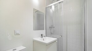 A bathroom with a white sink, a mirror, and a glass-enclosed shower. - Explore Lisbon from a Cozy Base in Alfama (Lisboa)