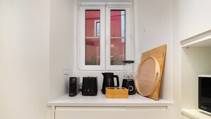 A kitchen with a white countertop, a window with a view of a red building, a blender, a toaster, and a wooden cutting board. - Explore Lisbon from a Cozy Base in Alfama (Lisboa)