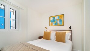 A neatly made bed with a beige quilt, two pillows, and a headboard with a framed artwork above it. - Explore Lisbon from a Cozy Base in Alfama (Lisboa)
