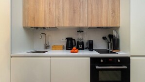 A modern kitchen with wooden cabinets, a sink, a blender, a kettle, and a stove. - Explore Lisbon from a Cozy Base in Alfama (Lisboa)
