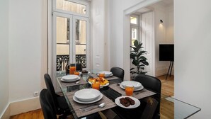 A dining area with a glass table, white plates, and orange juice. There are chairs and a potted plant.