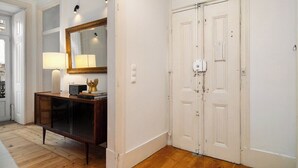 A room with a wooden floor, a white door, a white wall, and a wooden cabinet with a mirror and a lamp.