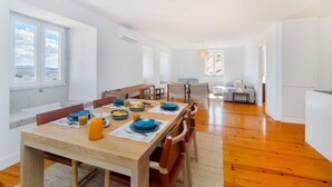 Ein geräumiger Essbereich mit einem Holztisch, gedeckt für das Frühstück, großen Fenstern mit Meerblick und einem hellen, luftigen Raum mit Sofa und kleinem Tisch.