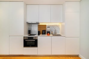 A modern kitchen with white cabinetry, a built-in oven, a coffee maker, and a marble backsplash.