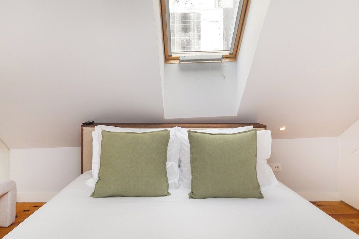 A bedroom with a skylight, a wooden headboard, and two green pillows.