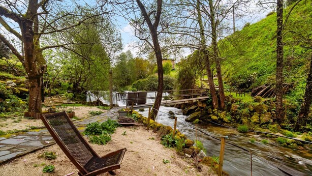 A bench overlooking a stream with a wooden bridge and a waterfall in the background. - Riverfront Retreat with Exclusive Waterfall Views (Baião)