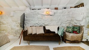 A cozy room with a stone wall, a brown sofa, a small wooden chair, and a flat-screen TV on a tripod. - Riverfront Retreat with Exclusive Waterfall Views (Baião)