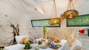 A dining area with a stone wall, a table set with various dishes, and hanging wicker lamps. - Riverfront Retreat with Exclusive Waterfall Views (Baião)