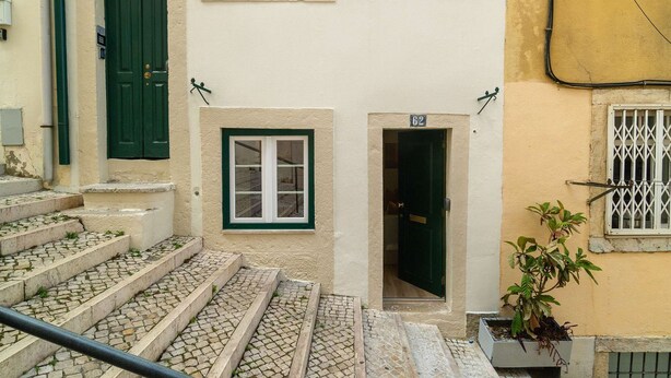 A staircase leading to a door with a number plate, a window with a grid pattern, and a potted plant on the right. - Modern Flat in Bica’s Historic Charm (Lisbon)