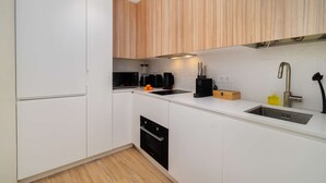 A modern kitchen with white cabinetry, a black microwave, a coffee maker, and a sink. - Modern Flat in Bica’s Historic Charm (Lisbon)