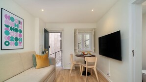 A living room with a sofa, a coffee table, and a TV mounted on the wall. - Modern Flat in Bica’s Historic Charm (Lisbon)