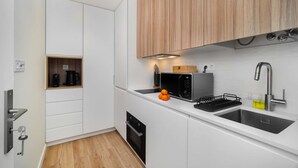 Une cuisine moderne avec des meubles blancs, un four encastré, un four à micro-ondes et un évier en acier inoxydable.