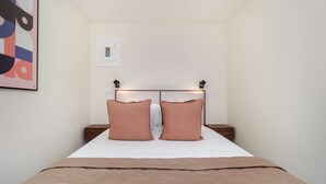 Une chambre à coucher comprenant un lit, deux tables de chevet, une tête de lit avec des lampes intégrées et un luminaire fixé au mur.