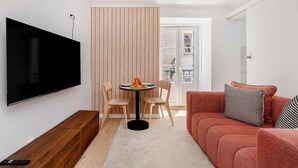 A living room with a flat-screen TV, a round dining table with chairs, a red sofa with patterned cushions, and a wooden partition. - Charming House in Bica Neighbourhood (Lisbon)