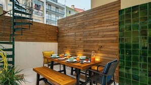 Un área de comedor al aire libre con una mesa y sillas de madera, rodeada por un muro de madera y un separador de vidrio verde.