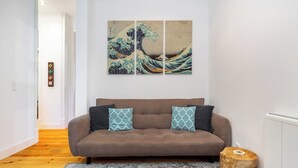 Una sala de estar moderna con un sofá marrón, cojines estampados, un tapete gris y una mesita de madera. Encima del sofá, cuelga una obra de arte tríptica.