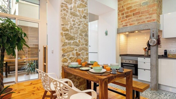 Una cocina moderna con pared de piedra, suelo de madera y comedor con mesa dispuesta para el desayuno.