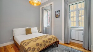 Un dormitorio con una cama, una colcha estampada, una lámpara colgante, una ventana con cortinas y un radiador.