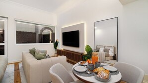 A modern living room with a sofa, a dining table set with plates, a TV mounted on the wall, and a large window. - Modern Studio in Santa Catarina (Porto)