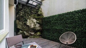 A patio with a table and chairs, a stone wall, and a hedge. - Modern Studio in Santa Catarina (Porto)