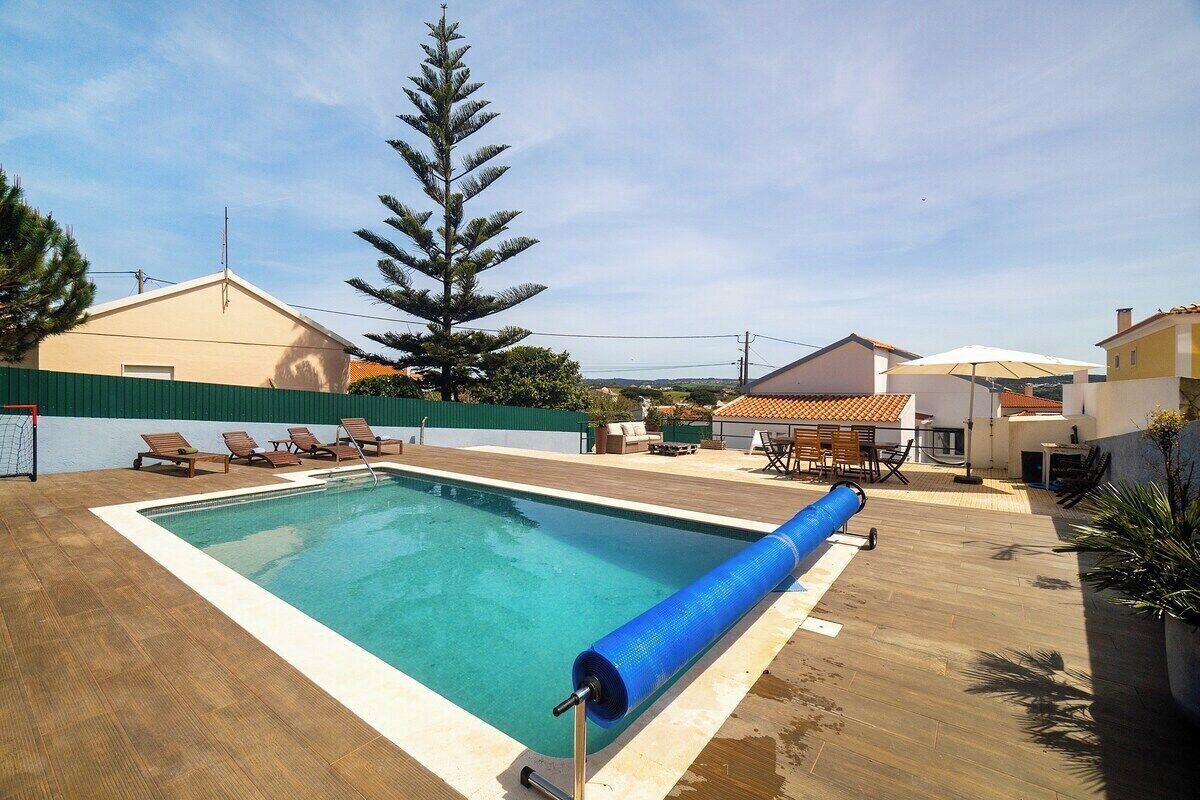A rectangular swimming pool with a blue water slide, surrounded by a wooden deck and lounge chairs.