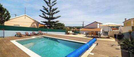 A rectangular swimming pool with a blue water slide, surrounded by a wooden deck and lounge chairs.