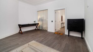 Una habitación amplia con piso de madera oscura, un mueble negro para televisión y una puerta blanca que da a otra habitación.