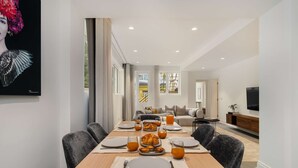 Un comedor moderno con una mesa larga dispuesta para el desayuno, con platos, vasos y una variedad de pasteles.