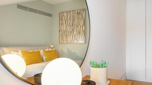Un salon moderne comprenant un canapé, un grand miroir, une table ronde avec une plante et une œuvre d’art abstraite accrochée au mur.