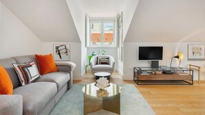 Un salon moderne comprenant un canapé, un fauteuil, une table basse, un téléviseur et des œuvres d’art.